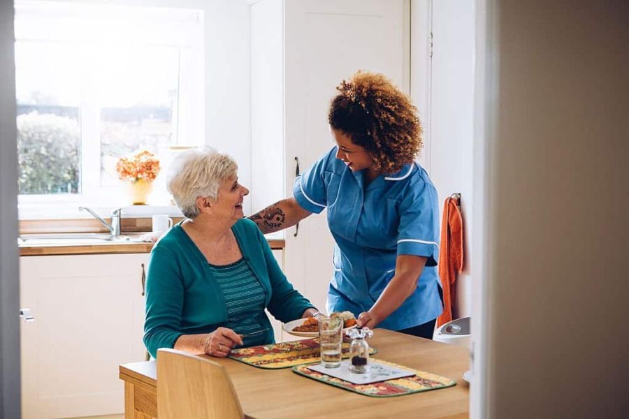 Care worker giving an old lady her dinner in her home.